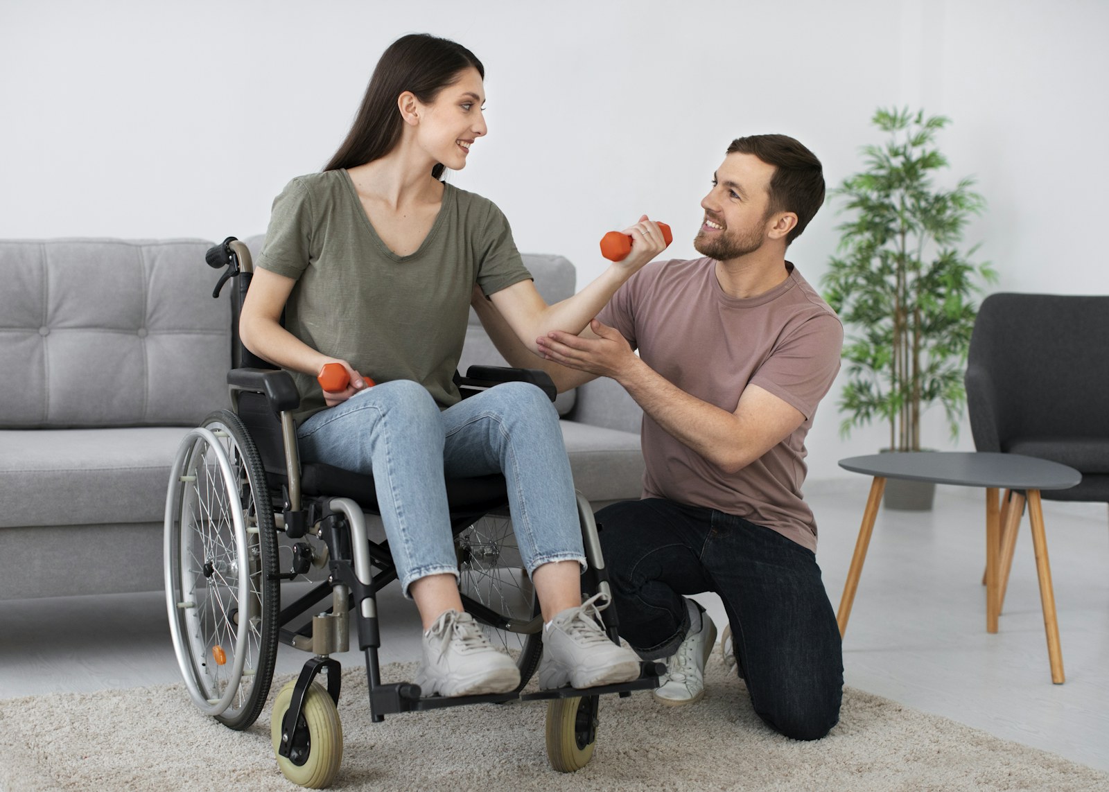 A support worker helping a woman in a wheelchair with a strength exercise at home